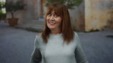 Hispanik son sınıf öğrencisi bir kadın canlı bir şehir sokak sahnesini işaret ediyor, açık şehir ortamında sıcacık gülümsüyor, pozitifliğini ve kendine güveni iletiyor..