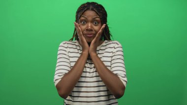 Elleri yanaklarına bastırılmış, geniş gözlü, ağzı açık yeşil perde stüdyosunda çizgili gömlek ve örgü takan bir kadın..