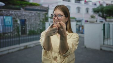 Gözlüklü genç sarışın kadın ve beline bağlanmış sarı gömlekli kadın caddeyi işaret ediyor..