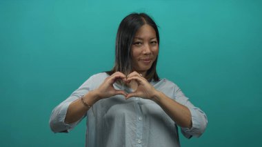 Gülümseyen kadın elleri ile bir kalp oluşturan stüdyo düzeyinde deniz mavisi arka planı ile; sevgi şefkat.