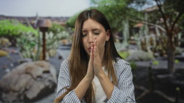 Ormanda çapraz kollarıyla kendine sarılan genç bir kadın yeşil kaktüs arka planıyla ve ağaçların arasından süzülen yumuşak güneş ışığıyla temizleniyor..