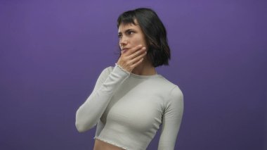 Eli çenesinde ve kaşları çatık parlak mor stüdyoda tefekkür eden genç İspanyol kadın..