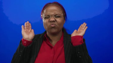 Afrika kökenli Amerikalı bir kadın mavi bir stüdyoda gözlük ve kırmızı bluz giyerken elleri ile gözlerini kapatır..