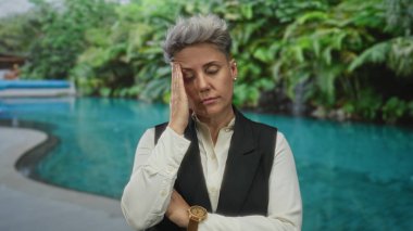 Beyaz gömlek ve siyah yelek giyen kadın, kapalı havuz güvertesinin yanındaki tapınakta dinleniyor..