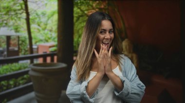 Kadın, görünür sarı tırnaklarla gülümserken güneşli bina terasında el çırpıyor; neşeli bir kutlama..