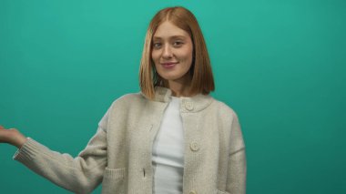 Elleri yeşil bir arka planda gülümseyen, bej bir kazak ve beyaz bir gömlek giyen, pozitifliği, kendine güveni ve sıradan bir tarzı olan bir kadın..