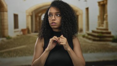 Gözlüklü ve kıvırcık saçlı bir kadın, eski bir kasaba caddesinde, duyguları, kültürü ve mimariyi ön plana çıkararak şaşırmış görünüyor..