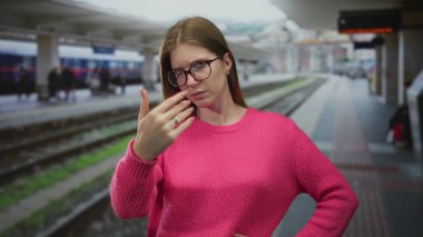 Pembe süveter giyen gözlüklü bir kadın inşaat platformunda kollarını kavuşturarak ayakta duruyor..