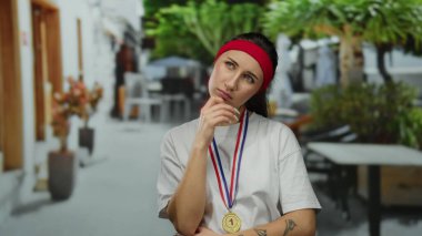 Şehir caddesinde, üzerinde madalya ve kırmızı saç bandıyla gezen bir kadın şehirli geçmişi olan, güneşli bir günde sportif ve düşünceli bir ruh hali içinde..