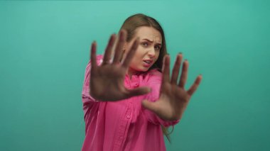 Pembe gömlekli kadın ellerini kaldırmış yeşil arka planda korku ya da kaygı belirtileri gösteriyor..