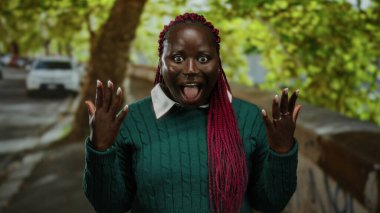 Pembe örgülü bir kadın, yeşil bir süveter içinde ağaçlar ve arabalarla dolu yemyeşil bir parkta dikilirken şaşkınlığını dile getiriyor..