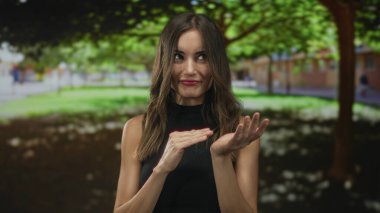 Yeşil bir orman parkında avuçlarında avuçlarıyla para harcayan bir kadın açık alandaki binaların yanında oyun oynuyor..