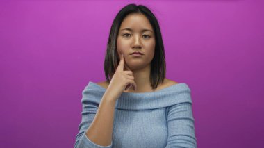 Parlak pembe bir duvarın karşısında mavi bir süveter giyen bir kadın izole bir arka planda tefekkür ve ifadeyi resmediyor..