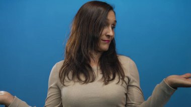 Mavi arka plan duvarına karşı belirsizlikle omuz silken bir kadın gündelik ve karışık bir ifade sergiliyor..