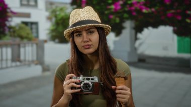 Dışarıdaki sokakta elinde kamera ve dondurma tutan bir kadın şapka takıyor, güneşli bir günde şehir sahnesinde gençlik yolculuğunu somutlaştırıyor..