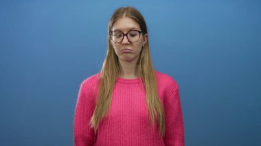 Pembe kazaklı ve yuvarlak gözlüklü genç kadın, stüdyoda çıplak yüzünü göstererek başını çeviriyor; can sıkıntısı iç gözlem.