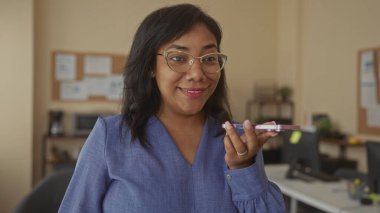 Modern bir ofis binasında akıllı telefonu ağzına doğru hoparlörle tutan kadın gülümseyerek cihaza doğru konuşuyor. Mutluluk..