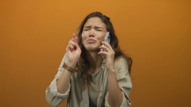 Telefondaki kadın umut dolu bir şekilde turuncu arka planda beklediği ve olumlu haber arzusunu dile getiriyor..