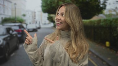 Şehir caddesinde bir kadını işaret eden uzun sarı saçlı, bej renkli bir kazak giyen bir kadın..