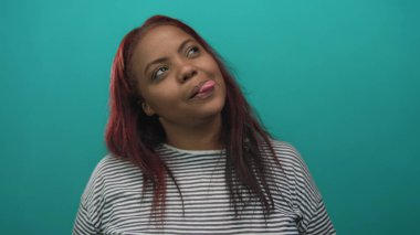 Çizgili tişörtlü, kızıl saçlı bir kadın stüdyo duvarlarıyla dil uzatıyor ve gülümsüyor..