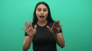 Avuç içleri açık ve elleri havada bir kadın, yeşil bir stüdyo ortamında ağzı açık, kameraya dönük; sürpriz dikkat alarmı..