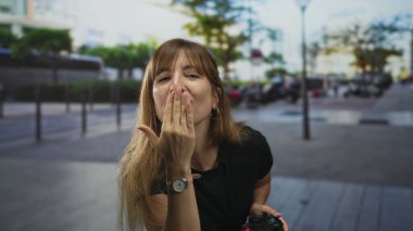 Kadın, şehir caddesinde bir oyun kumandasını tutarken el pençe dize öpüşüyor; neşeli bir selamlama..