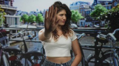 Avuç içi dışarıda bir kadın Amsterdam 'da bir kanal köprüsü caddesinde beyaz bluz ve kot pantolon giyerek duran jesti durdurun..