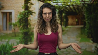 Çıplak kollu genç İspanyol kadın güneş ışığında kırsal bir binanın yanında omuz silkiyor..