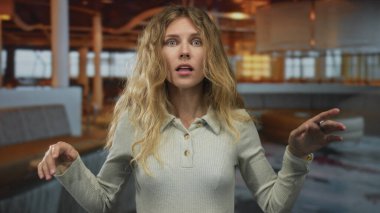 Kadın elini kaldırıyor, sallanıyor, sarışın genç bir figür gibi modern gündelik bir ortamda şaşırmış bir ifadeyle sesleniyor..