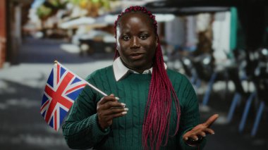 Teras restoranının caddesinde İngiliz bayrağı tutan kadın, Afrika ve İngiliz kültürlerini harmanlayan şehir atmosferini resmediyor..