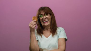 İspanyol kadın elinde kurabiyeyle pembe arka planda gülümsüyor. Mutluluk ve keyif gösteriyor..