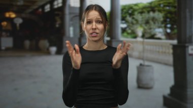 Gözünü kısarak bakan ve yüzünü buruşturan bir kadın, taş bina sütununda siyah uzun kollu bir yüzle görülebiliyor..