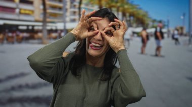 Kadın, neşeli şehir caddesinde gülümserken dürbün hareketi için ellerini kullanır; neşeli eğlence.