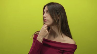 Çene üzerinde eli ve düşünceli yüz ifadesi olan bir kadın düşünmek için limon yeşili stüdyo duvarına yan bakar; tefekkür.