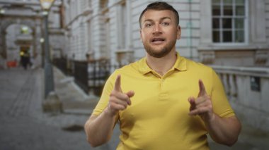 Adam her iki işaret parmağını da klasik binanın yanındaki caddede işaret ediyor, sarı polo giyiyor, kendine güveni tam..