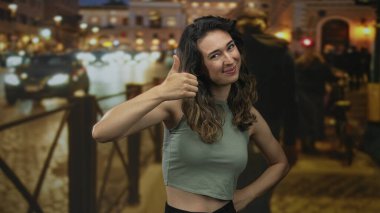 Gece yarısı şehir caddesinde trafik ışıkları bulanık ve geçen arabalarla sıcak sokak lambalarının altında baş parmak gösteren kadın iyimserlik.