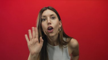 Kadın, kırmızı bir stüdyoda, halka küpeli, dudaklı ve geniş gözlü çıplak elini kaldırır..