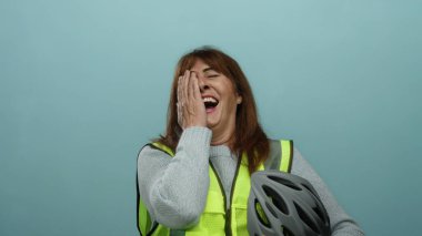 Üst düzey İspanyol kadın, elinde mavi duvar arkası kaskla neşeyle gülüyor, güvenlik bağlamında mutluluk ve mizah iletiyor..