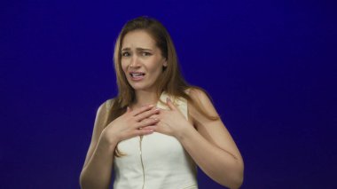 Mavi bir stüdyoda beyaz bir elbise giyen korkmuş yüz ifadesi olan beyaz bir kadın, korku..