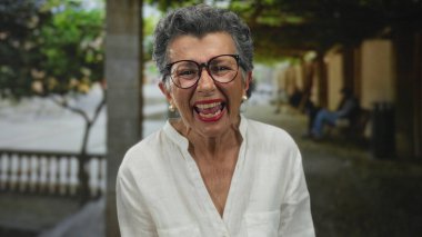 Yaşlı, gri saçlı bir kadın, eski bir kasaba caddesinde neşeyle gülüyor, şehir ortamında canlı yüz ifadesi ile ilgi çekici bir sahne yaratıyor..