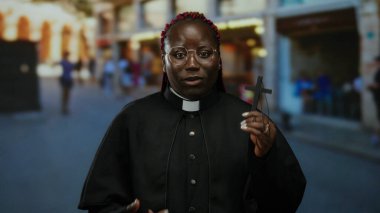 Şehir caddesinde haçı olan kadın rahip şehir ortamında inanç ve maneviyat aktarıyor, çeşitliliği ve dini bağlılığı vurguluyor..