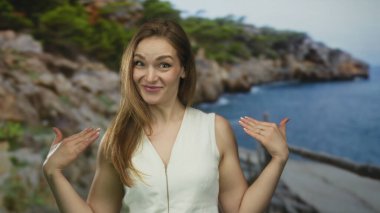 Beyaz kolsuz üst giyen kadın, kayalık kıyı şeridine bakan orman yolunda ahşap korkuluklardan palmiyeler tutuyor..