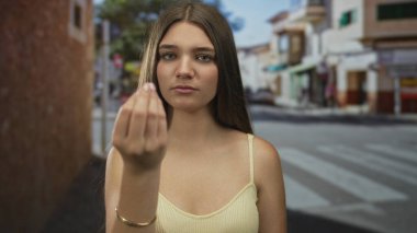 Sarı kolsuz tişörtlü genç kız, zebra caddeden geçmeden önce el hareketleriyle parmaklarını çimdikliyor.
