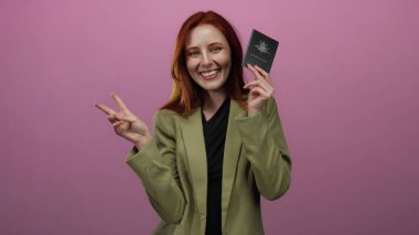Avustralya pasaportlu gülümseyen bir kadın seyahat heyecanını temsil eden pembe arka plana karşı zafer jesti sergiliyor.
