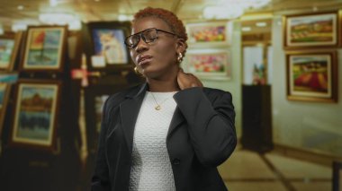 Siyah ceketli kadın, sanat galerisinde boynu beyaz duvarlarda çerçeveli resimlerle dolu, rahatsız..