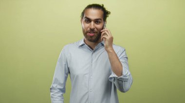Telefonda konuşan genç bir adam, hafif bir gülümseme ve sakallı, limon yeşili bir stüdyoda düğme gömlekli, düşünceli bir odak noktası..