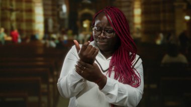 Kilisenin içinde bileğini tutan Afrikalı Amerikalı bir kadın vaaz sırasında acı çekiyor. Arka planda bulanık bir cemaat var. Gözlük ve örgü takıyor..