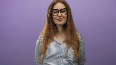 Kızıl saçlı, gözlüklü ve çizgili tişörtlü bir kadın stüdyoda gözlerini kırpıyor ve nazikçe gülümsüyor..