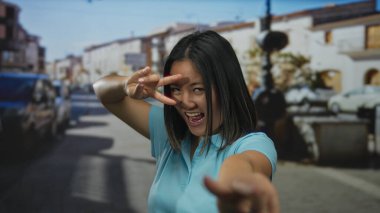 Çinli bir kadın şehir caddesinde neşeli bir zafer jesti yapıyor. Canlı bir ifadeyle ve şehir geçmişiyle kamerayı işaret ediyor..