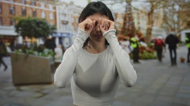 Genç İspanyol kadın gün ışığında hareketli bir şehir caddesinde dururken gözlerini ovuşturur ve gülümser;.